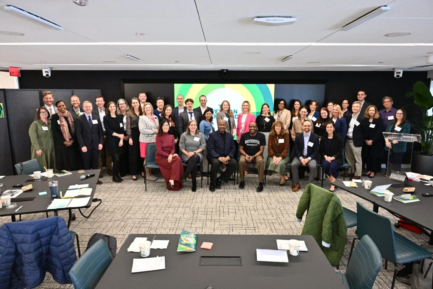 group of people posing together in a conference room with a screen in the background.